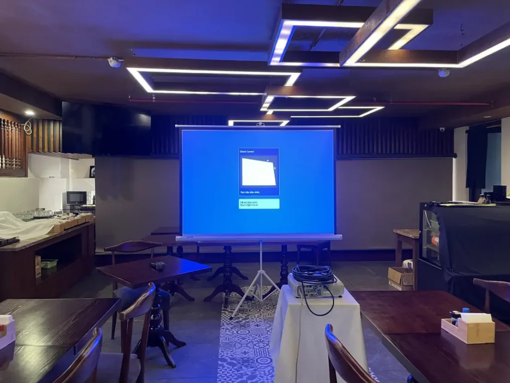 phòng họp hiện đại với màn hình chiếu và bàn ghế gỗ, trang bị thiết bị âm thanh và ánh sáng LED